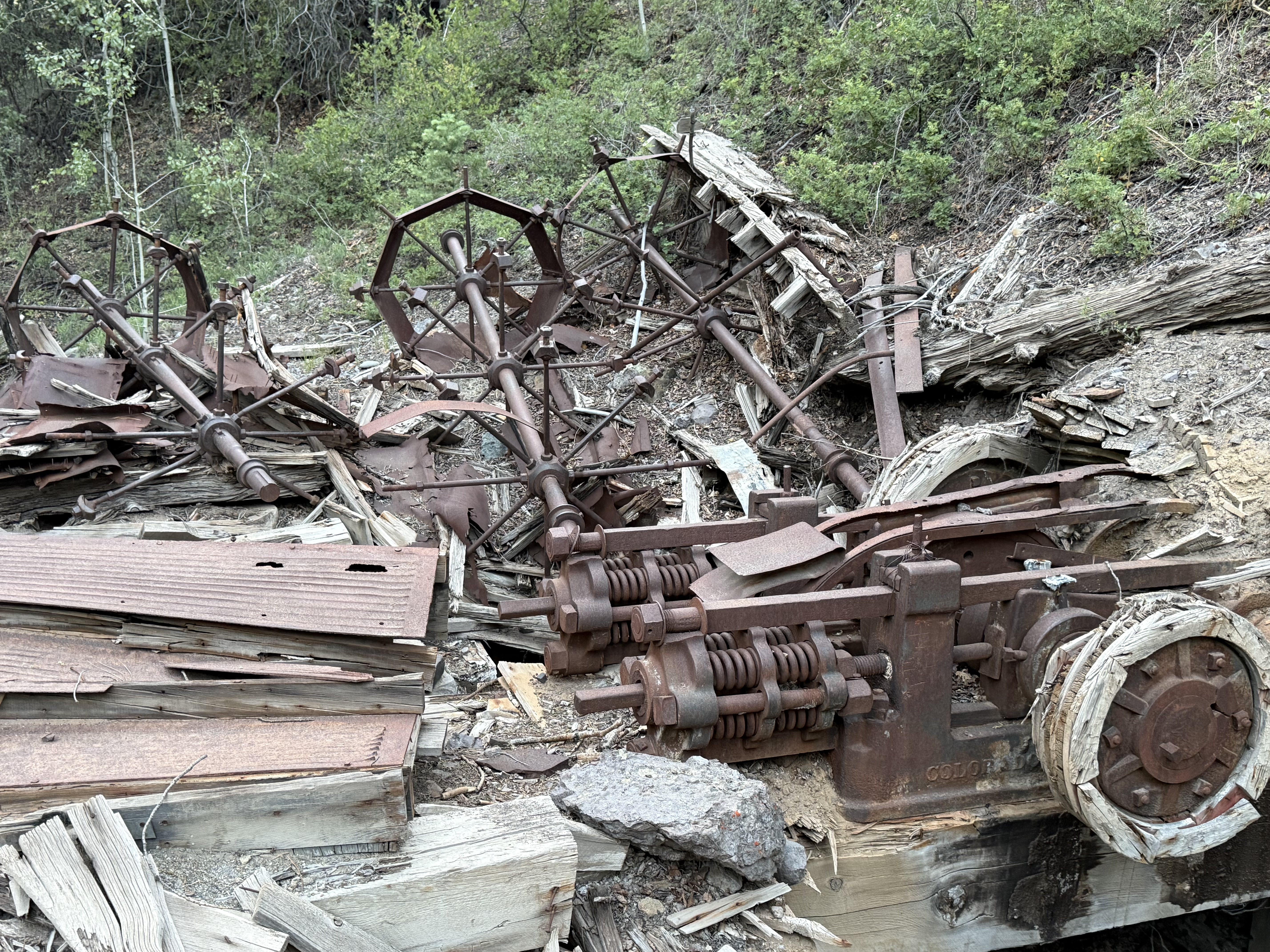 Collapsed mine timber and rusted ore-cart trucks scattered on a hillside in the San Juan Mountains, Colorado