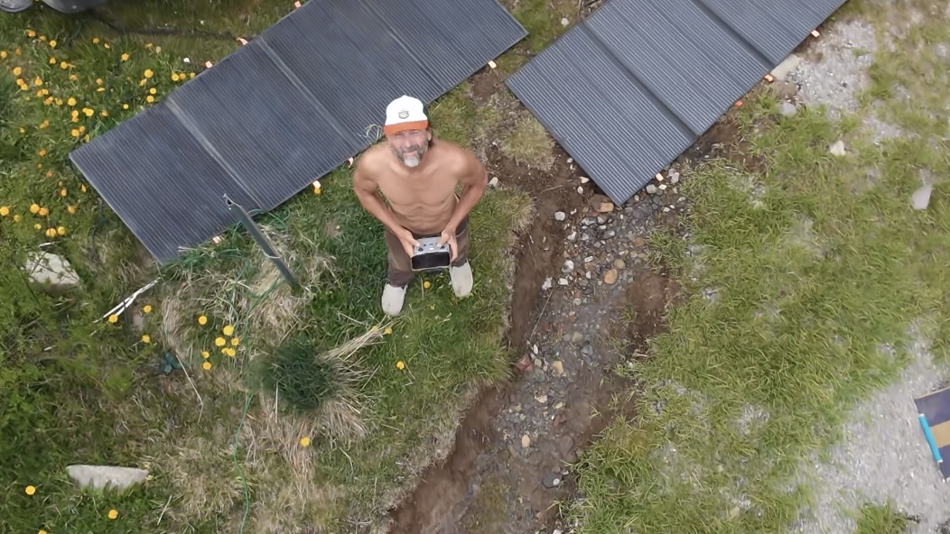 Aerial drone shot looking down at Layng standing between solar panels beside his Sprinter van, San Juan Mountains, Colorado.