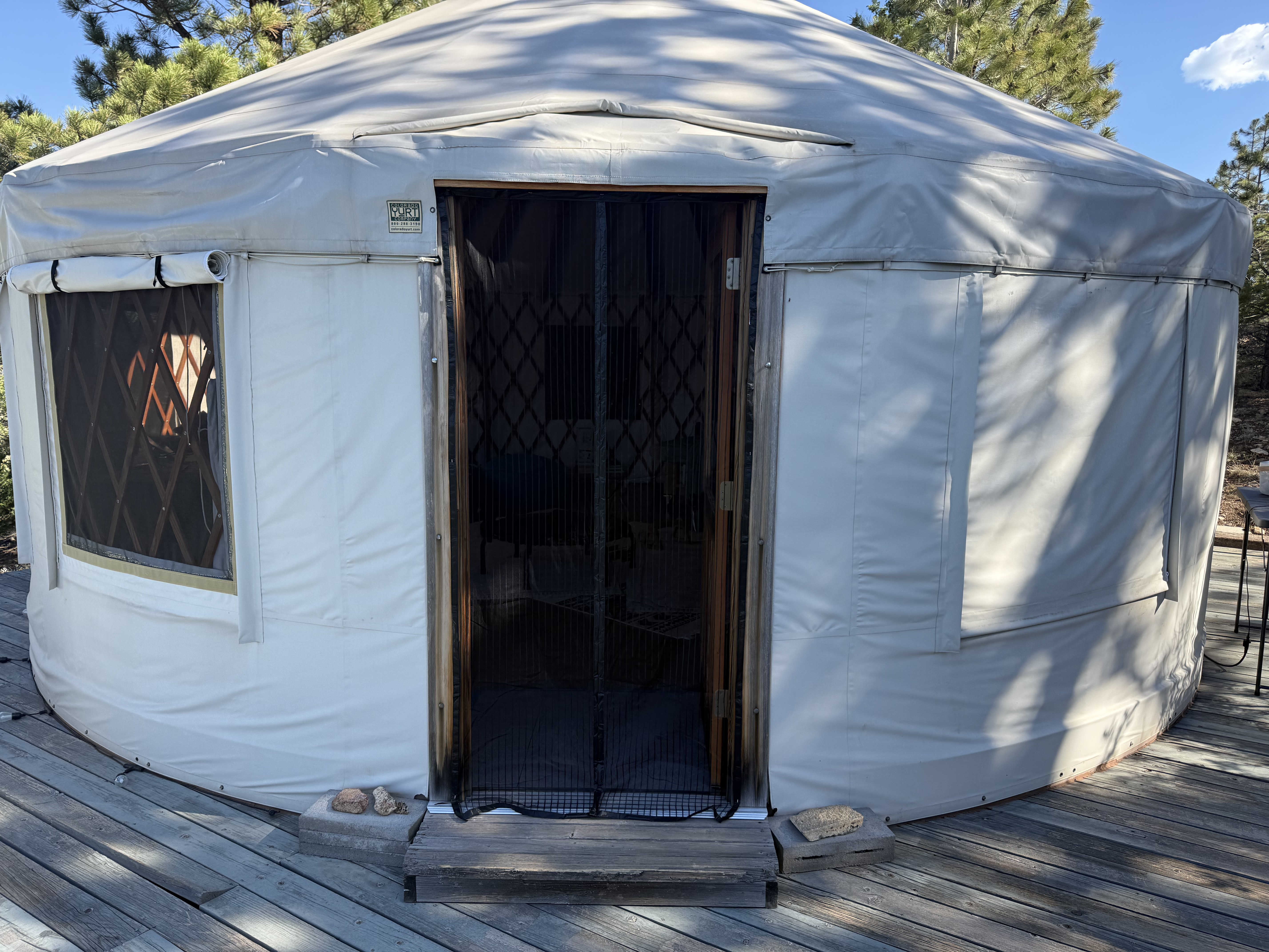 The yurt on its deck above Telluride, Colorado, screen door open, surrounded by pine trees under a clear blue sky