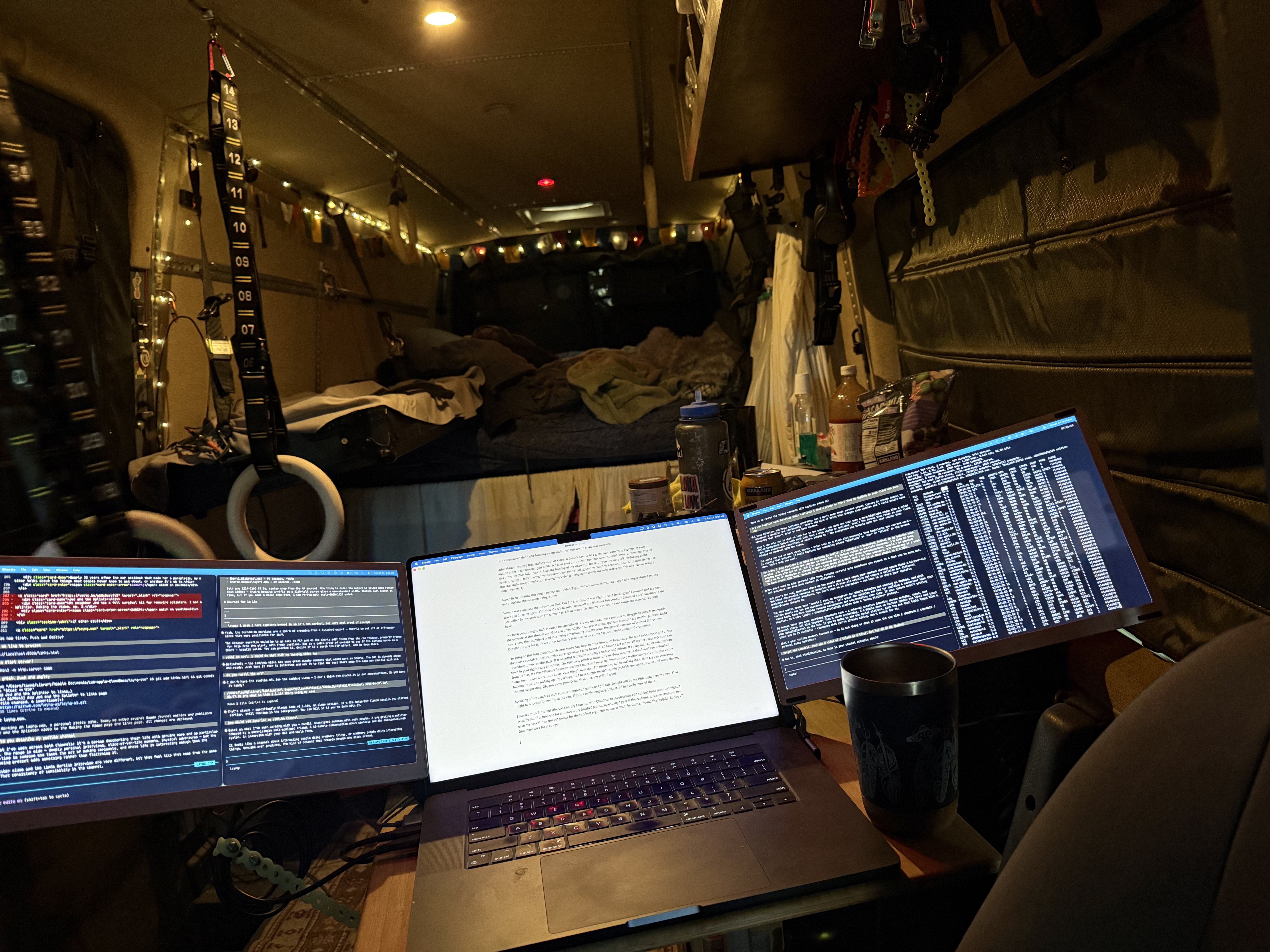 Three screens glowing in the van at night: code, document, data. Fairy lights and gear in the background.