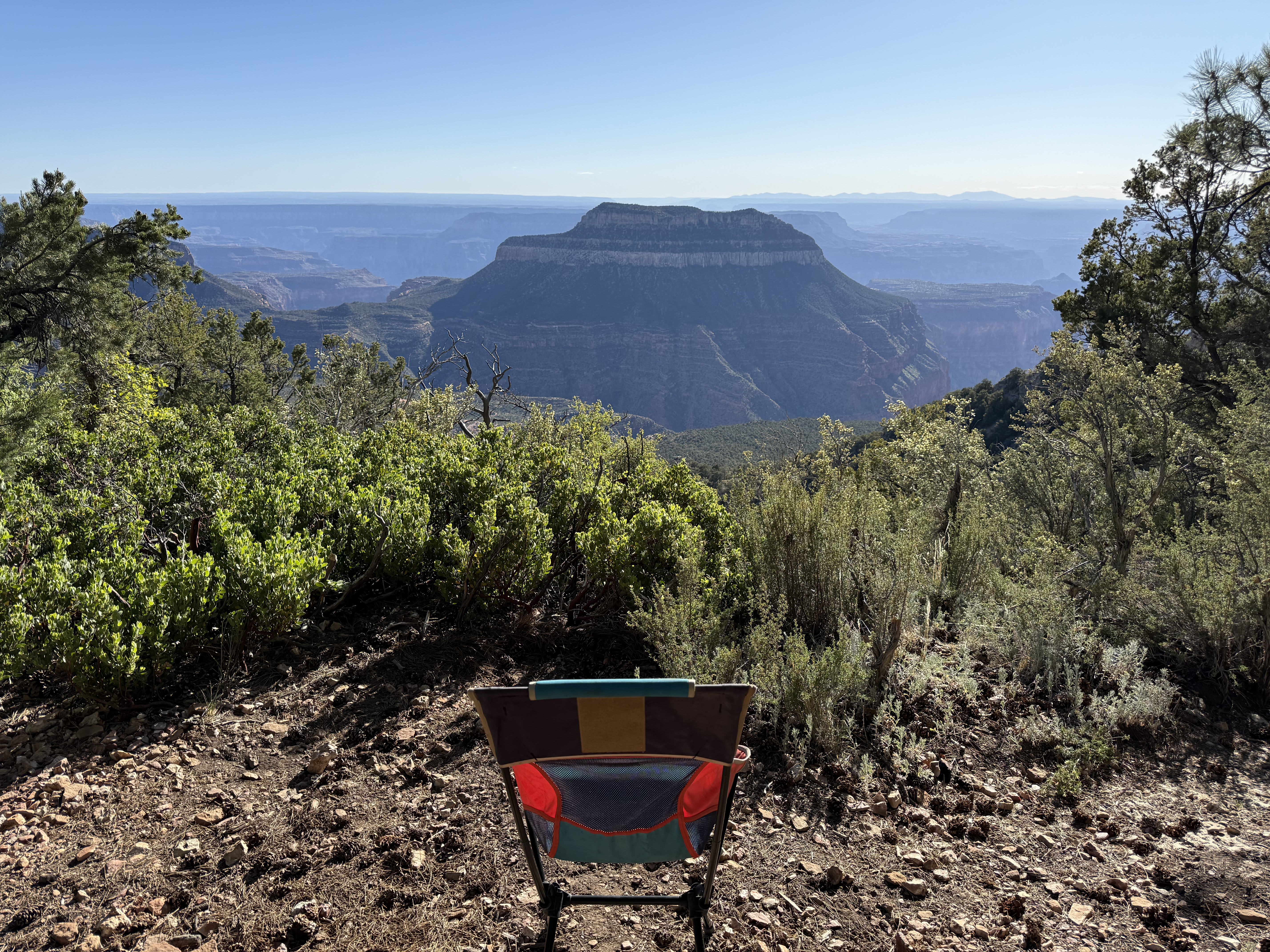 Camp chair facing the Grand Canyon from the North Rim, a flat-topped mesa rising from the canyon below, blue sky above