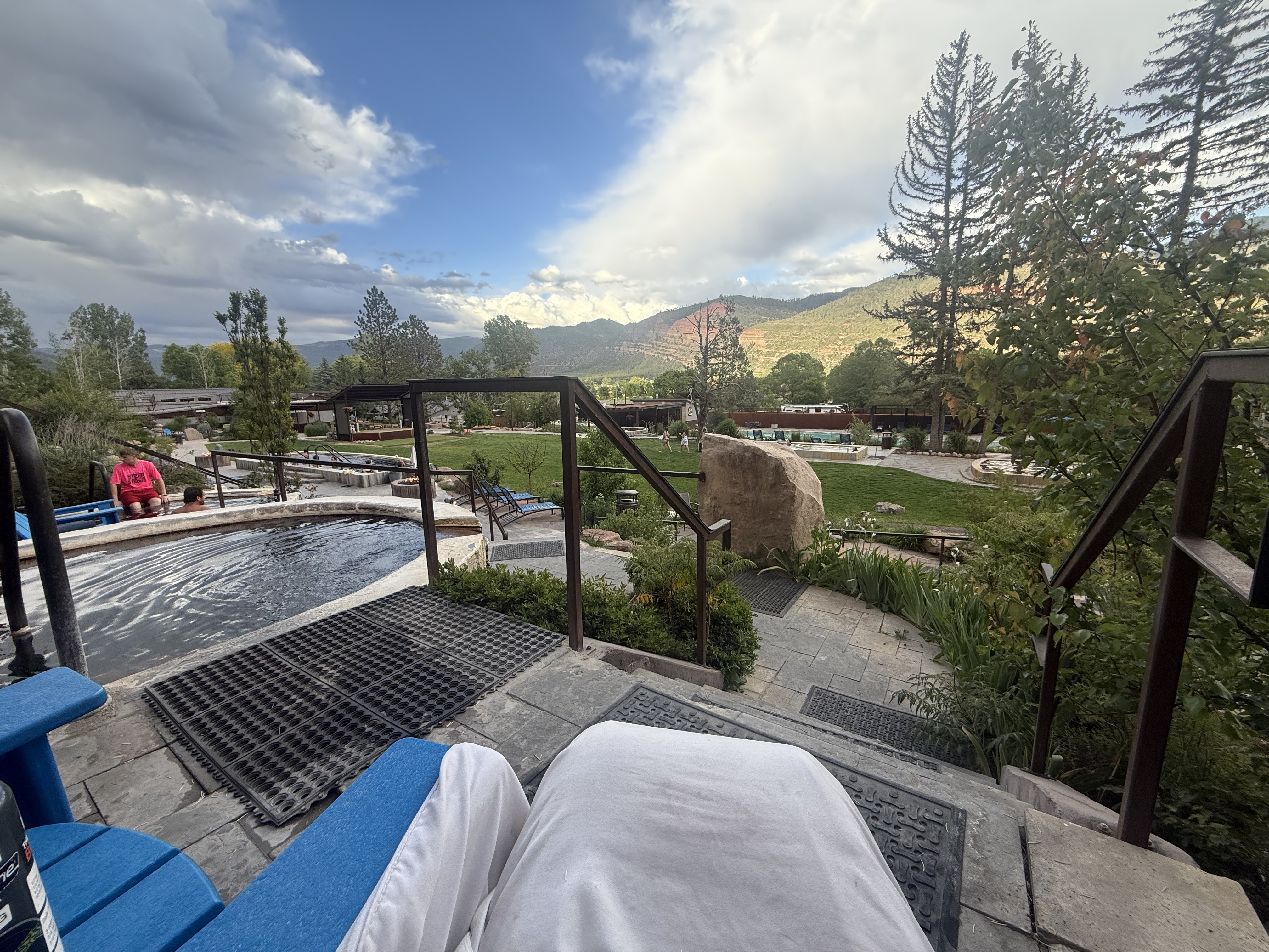 Hot springs near Durango, Colorado. View from a lounge chair over the cold plunge pool, with pine trees and red rock mountains in the background.