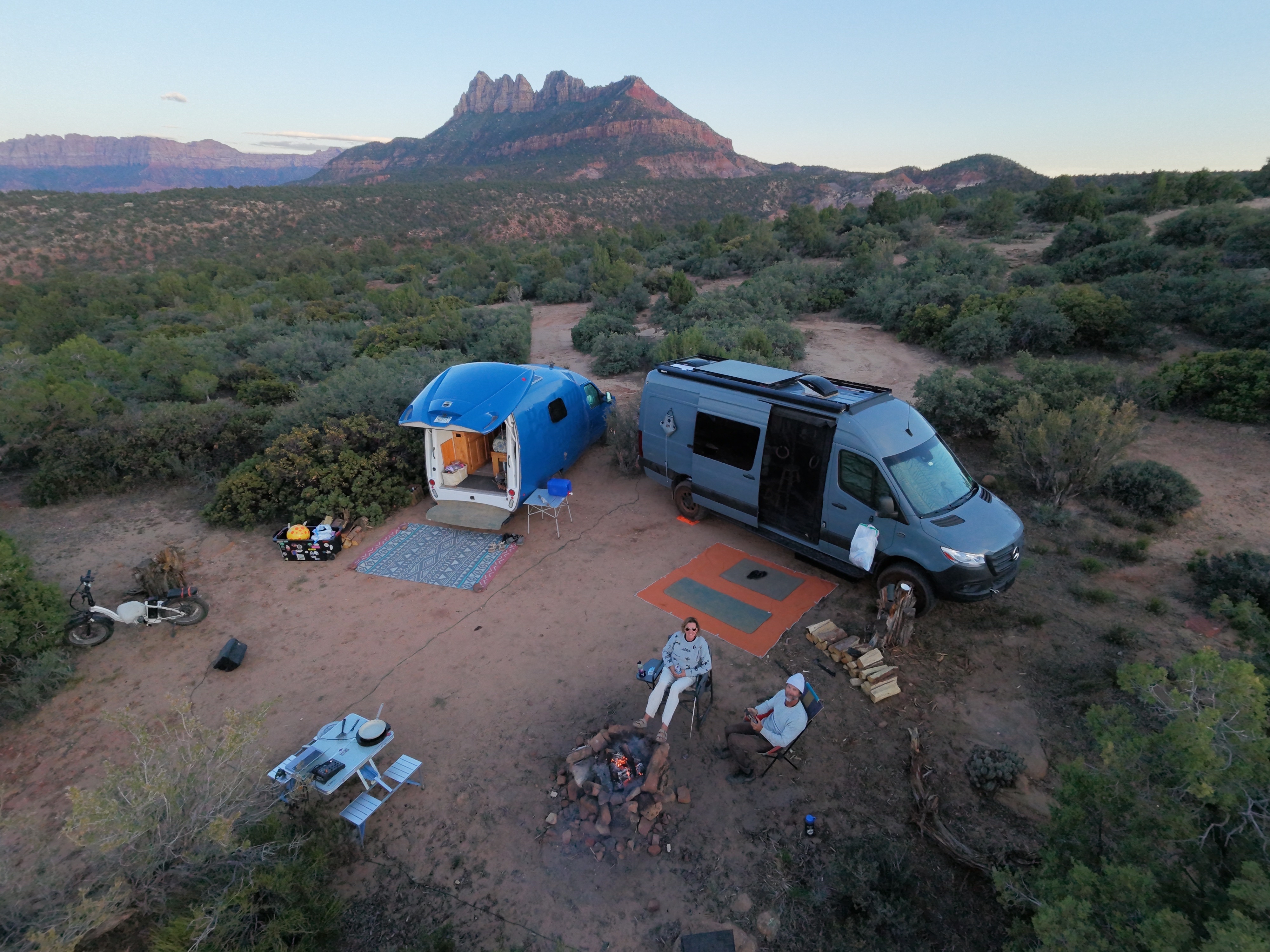 Drone shot of two rigs and a campfire at sunset, Zion peaks behind, Southern Utah