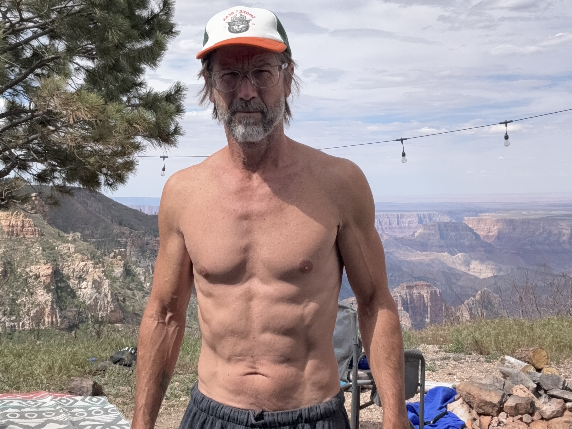 Shirtless at camp on the North Rim, Grand Canyon visible behind, string lights overhead