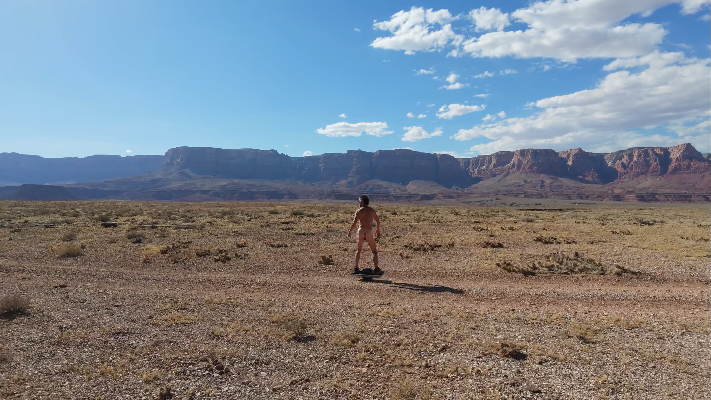 Riding the OneWheel naked across the desert with canyon walls behind