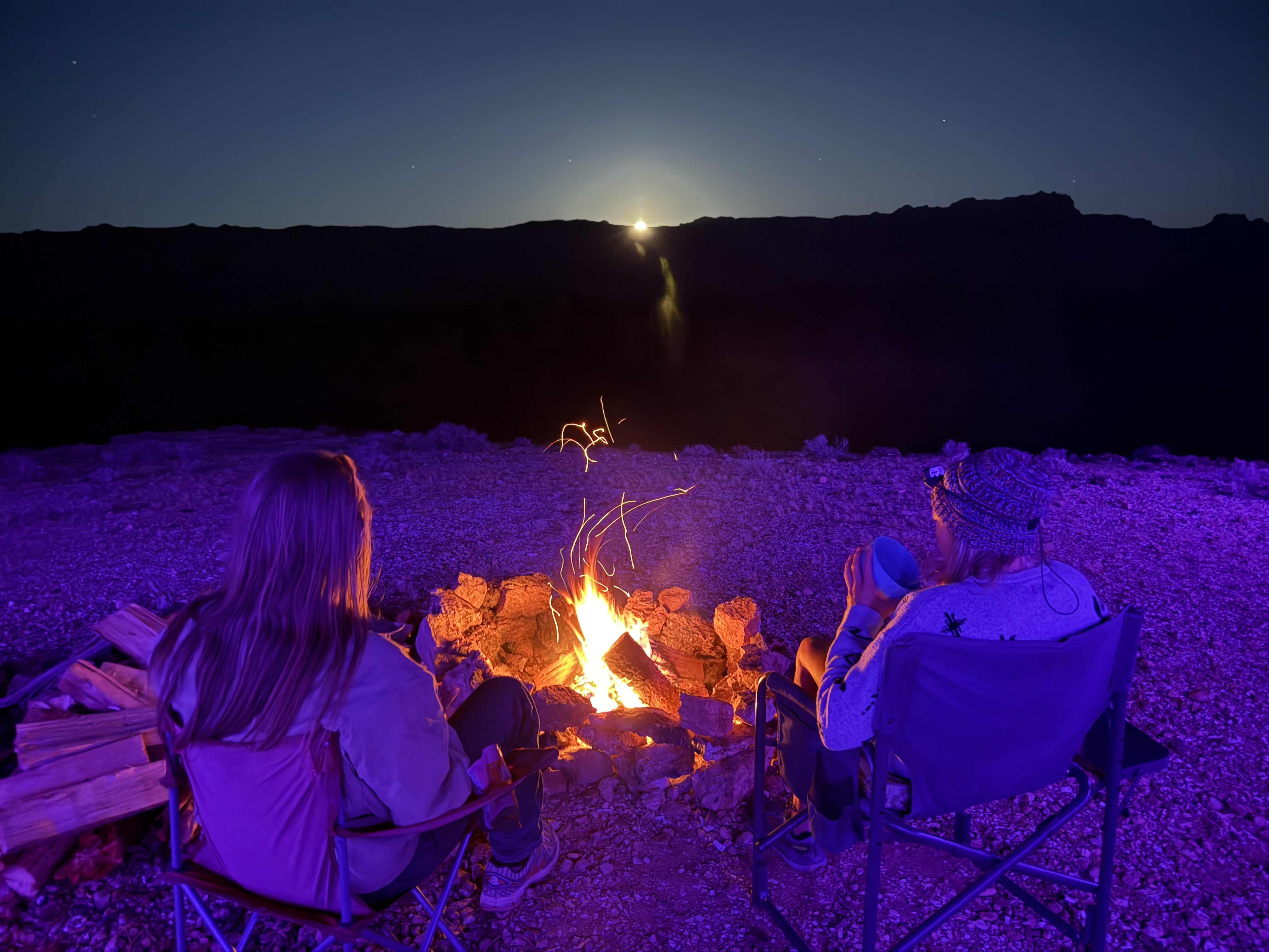 Campfire at night with full moon rising over the canyon rim, Arizona Strip