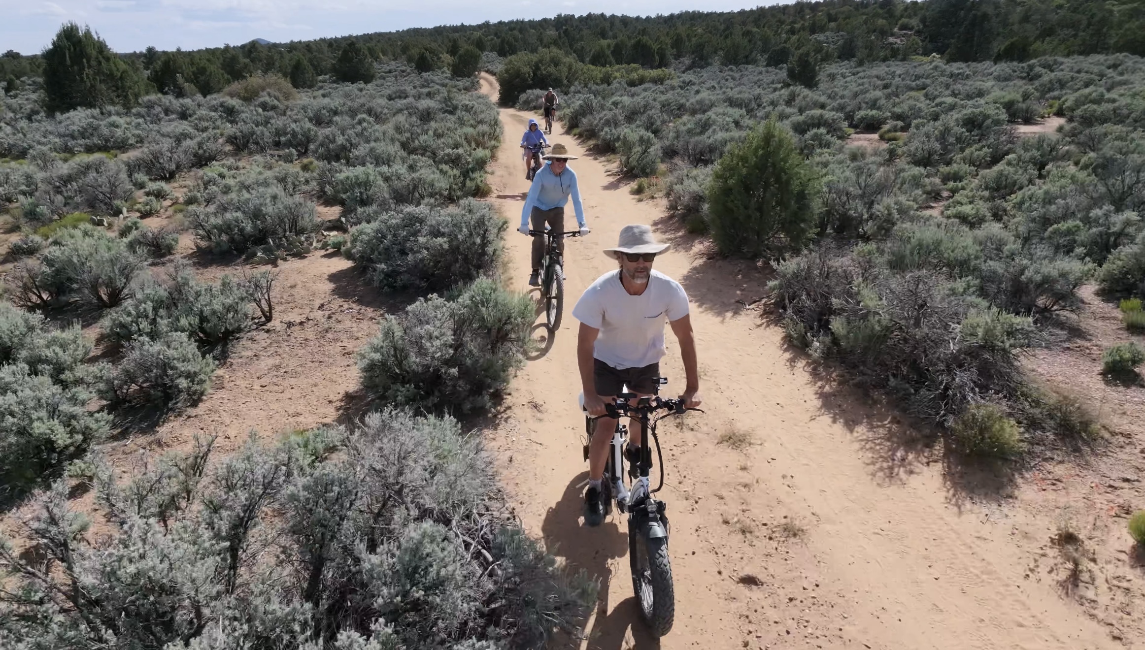 Drone shot of three riders on fat bikes along a desert trail through sage, Southern Utah