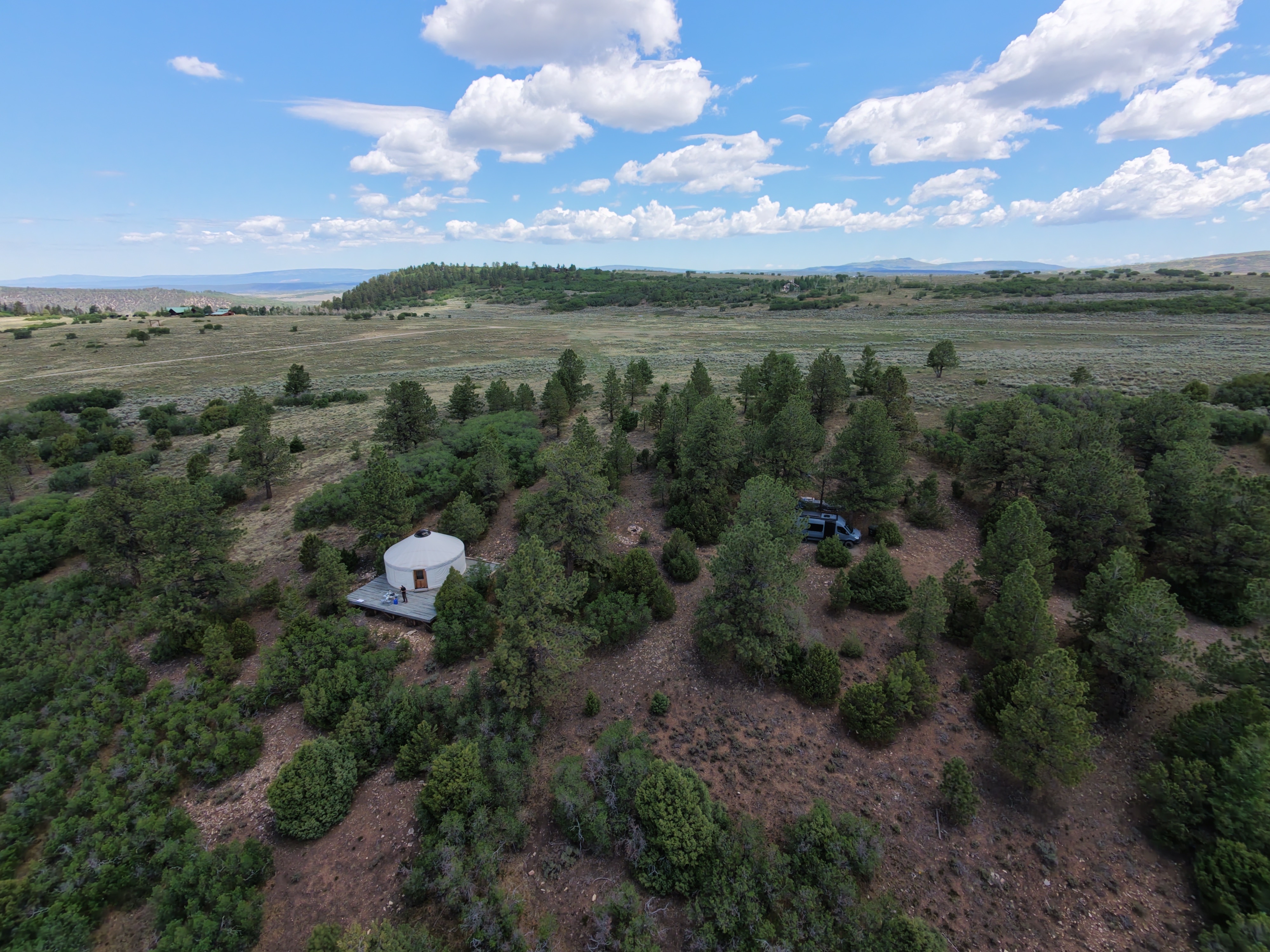 Aerial drone shot of the yurt and Sprinter van on a property above Telluride, Colorado, surrounded by pine trees and mountain views.