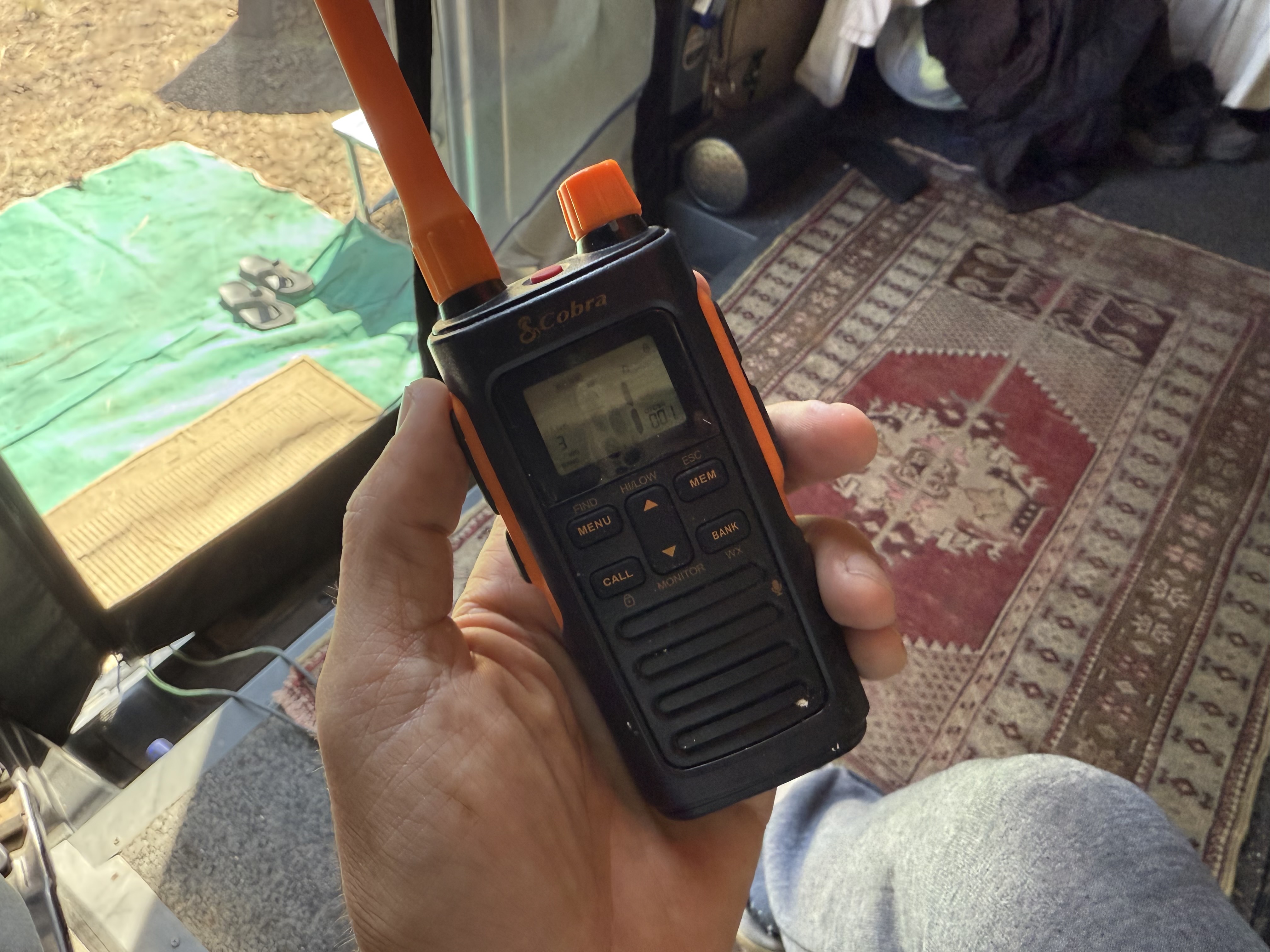 Holding a Cobra walkie talkie, van interior and camp visible behind